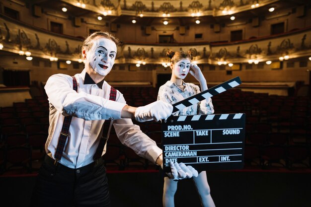 Smiling male mime artist holding clapperboard in front of female mime on stage