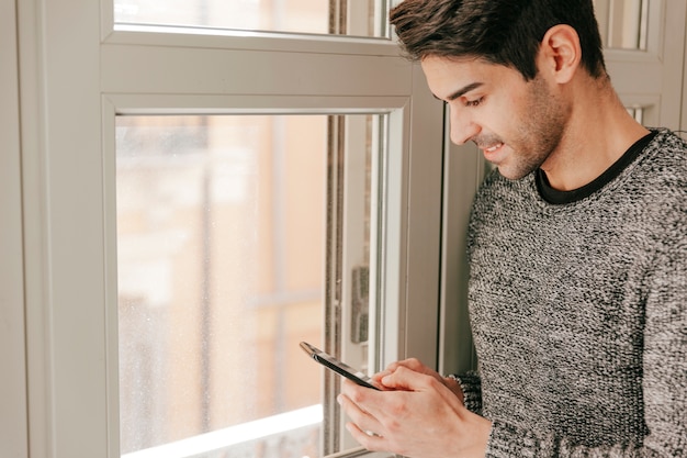 Free photo smiling man browsing smarthone near window