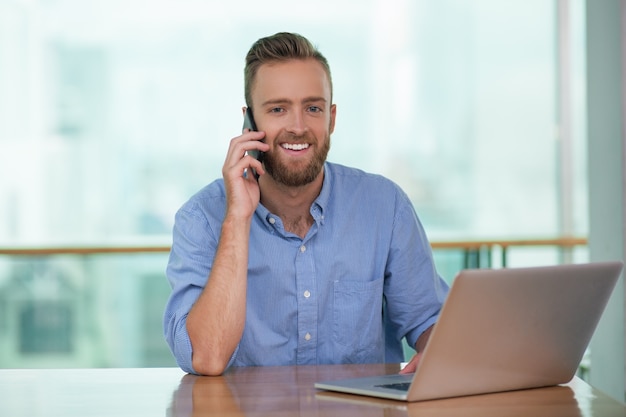 Smiling Man Calling on Phone and Working on Laptop