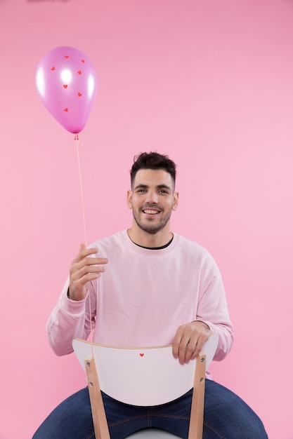 Free photo smiling man on chair holding violet balloon