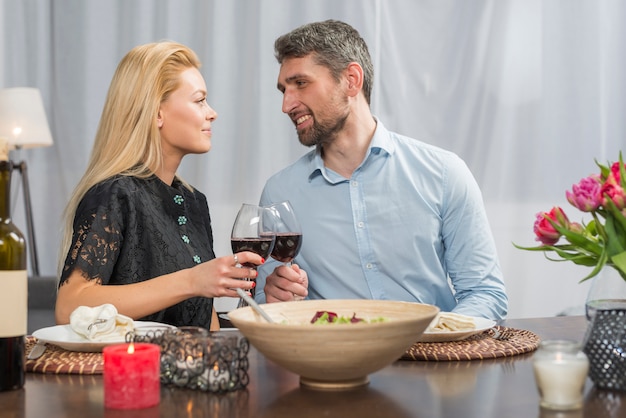 Smiling man clanging glasses of wine with woman at table 