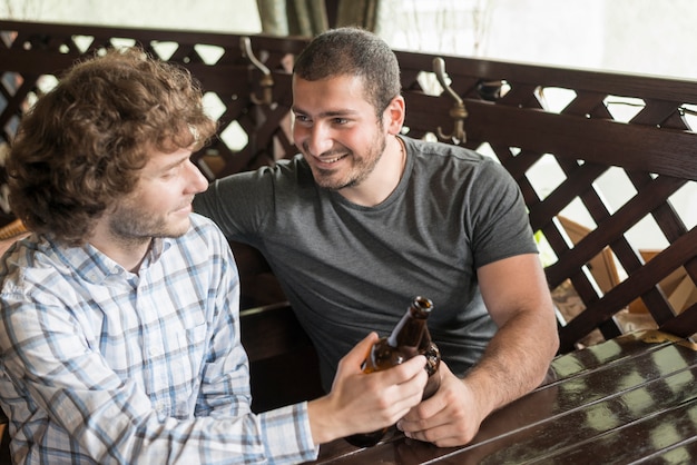 Smiling man clinking bottles with friend in bar