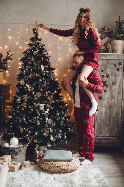 Smiling man holding beautiful wife on his shoulders on Christmas eve