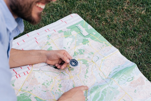 Free Photo smiling man holding compass and pointing at map on grass