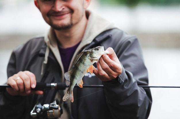 Smiling man holding fishing rod showing caught fish