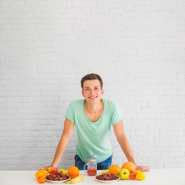 Smiling man leaning on desk with many colorful fruits