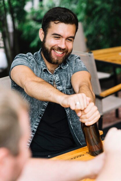 Smiling man opening the alcohol bottle sitting in the restaurant