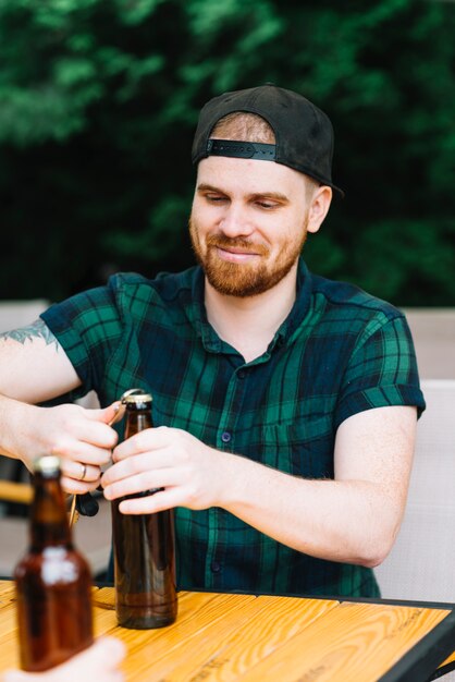 Smiling man opening the bottle cap with opener on wooden table