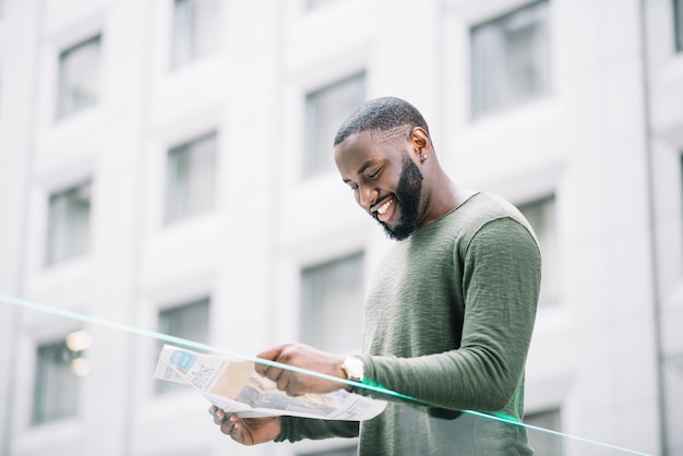 Free photo smiling man reading newspaper near glass fence