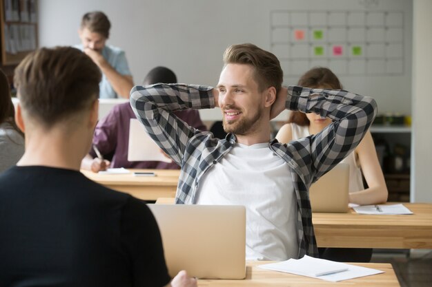 Free Photo smiling man relaxing hands behind head enjoying work in co-working