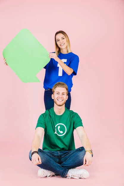 Free photo smiling man sitting in front of woman holding empty green speech bubble