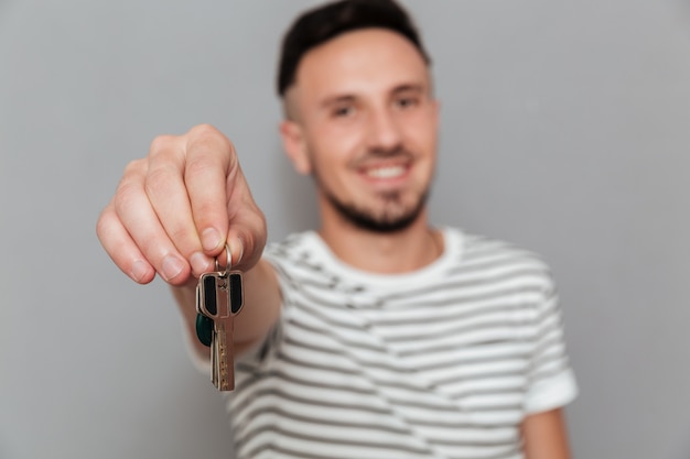 Free photo smiling man in t-shirt showing keys at the camera