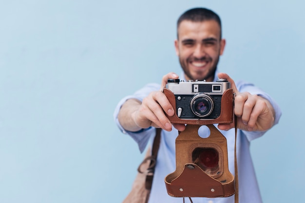 Smiling man taking photo with retro camera standing against blue wall