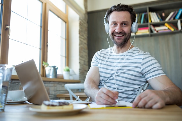 Smiling man with headphones writing in his diary at coffee shop