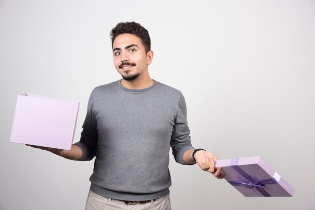 Smiling man with an opened purple box over a white wall.