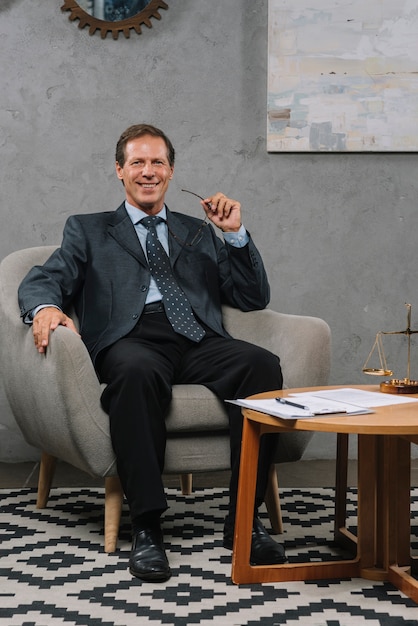 Free photo smiling mature businessman sitting on soft armchair