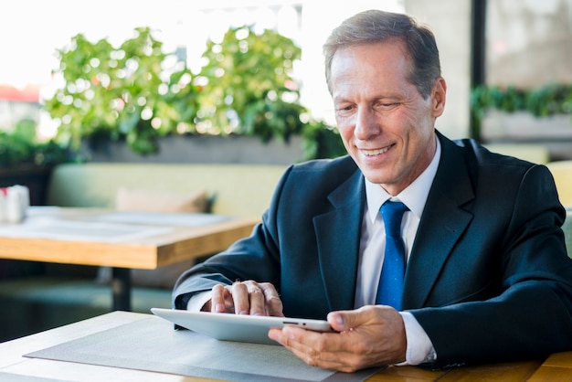 Free photo smiling mature businessman working on digital tablet in restaurant