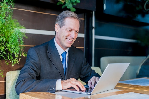 Free Photo smiling mature businessman working on laptop over desk in restaurant