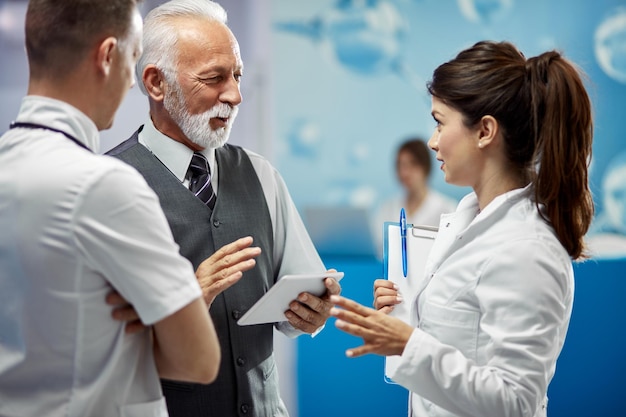 Smiling mature financial advisor and doctors communicating while standing in a lobby at medical clinic