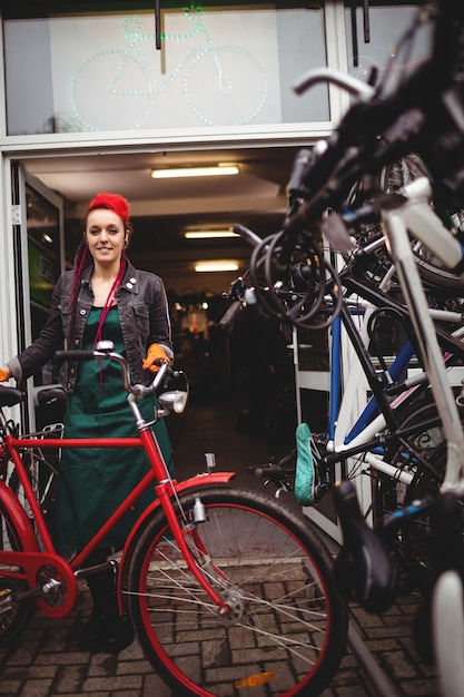 Smiling mechanic standing with a bicycle in workshop