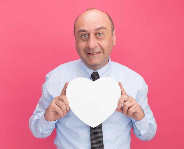 Free photo smiling middle-aged man wearing white t-shirt with tie holding heart shape box isolated on pink wall