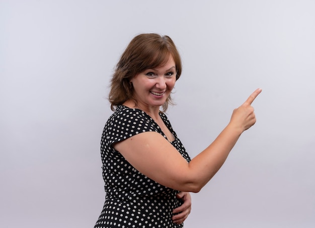 Smiling middle-aged woman pointing with finger at right side on isolated white wall