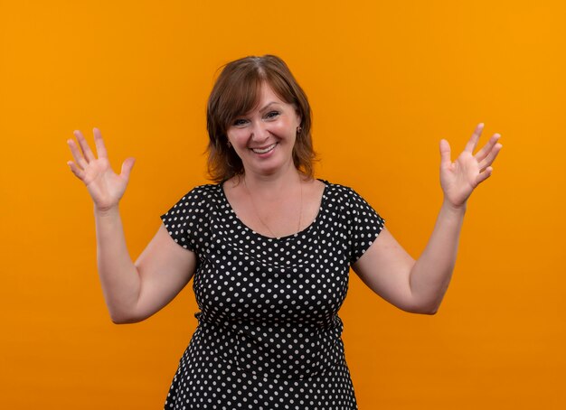 Smiling middle-aged woman with lifted hands on isolated orange wall