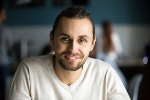 Smiling millennial man looking at camera in cafe, headshot portrait