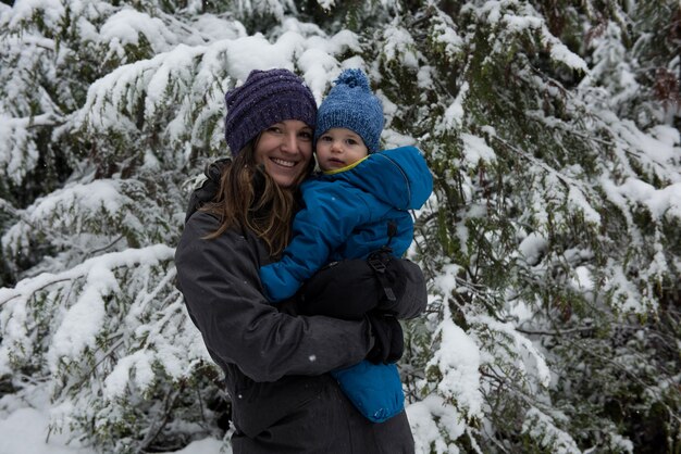 Smiling mother carrying son against snow covered trees