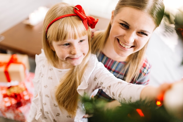 Smiling mother and daughter decorating christmas tree together