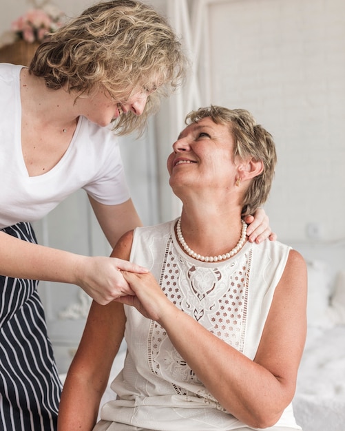 Smiling mother and daughter looking at each other and holding hand at home