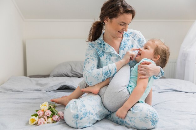 Smiling mother and daughter playing on bed