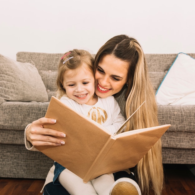 Free photo smiling mother and daughter reading book near couch