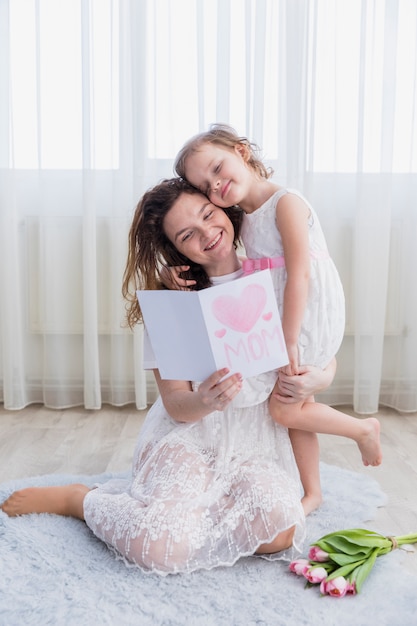 Free photo smiling mother and daughter reading mother's day card together at home