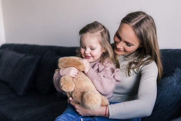 Free photo smiling mother hugging cute little girl holding teddy bear toy showing love and care in family