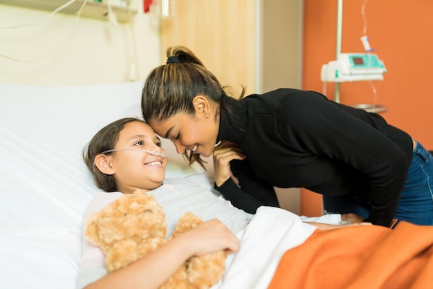 Smiling mother and unwell daughter by bed at hospital during visit