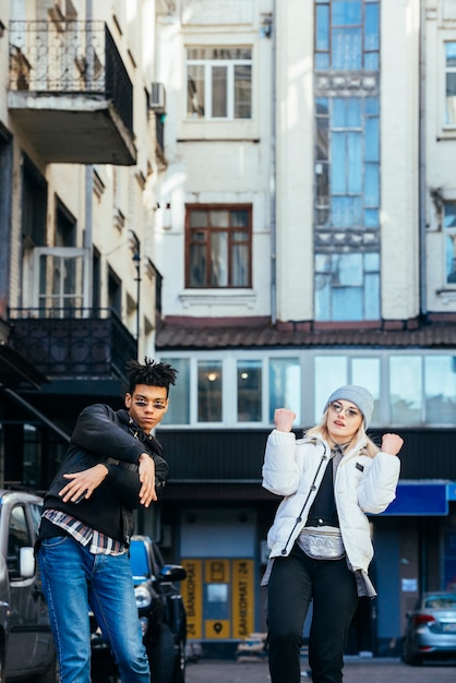 Free photo smiling multi ethnic young couple standing under the building dancing on street