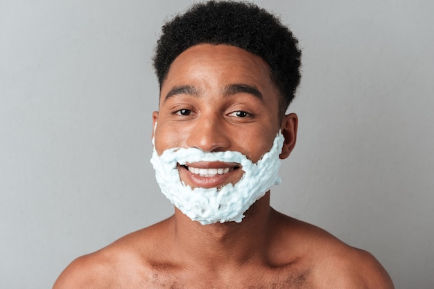 Smiling naked african man with face in shaving foam