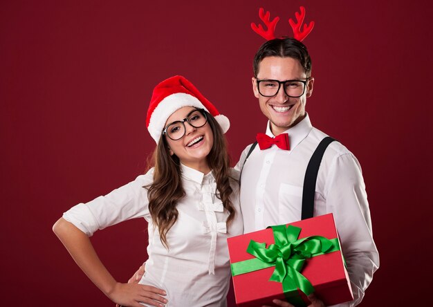 Smiling nerd couple holding red christmas gift