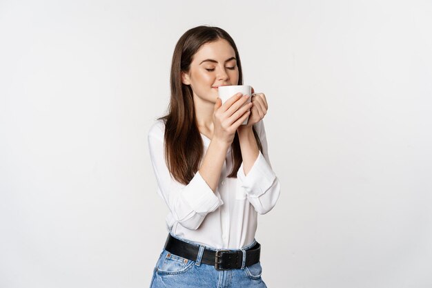 Smiling office woman drinking coffee, drink from mug with satisfaction, pleasure, standing over white background