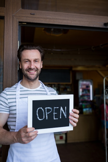 Free photo smiling owner holding a open sign at bakery shop entrance