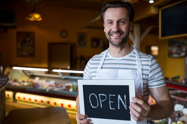 Free photo smiling owner holding a open sign in the bakery shop