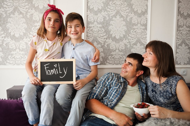 Free Photo smiling parent looking at their children holding slate with family text