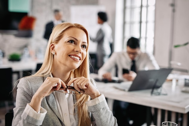 Free Photo smiling pensive businesswoman day dreaming while being at work there are people in the background