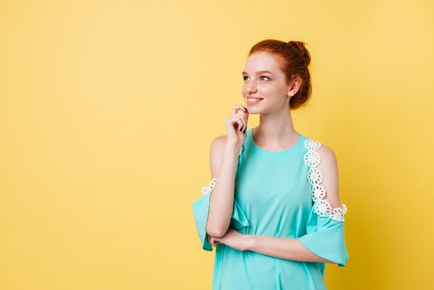 Smiling pensive ginger woman in dress holding her chin