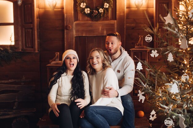 Smiling people sitting on wooden porch in front of door with Xmas wreath