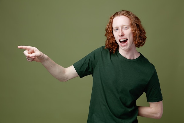 Smiling points at side young handsome guy wearing green t shirt isolated on green background