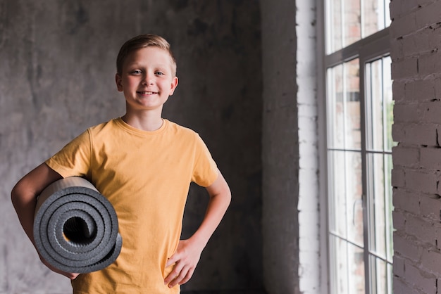 Free Photo smiling portrait of a boy holding grey rolled up exercise mat