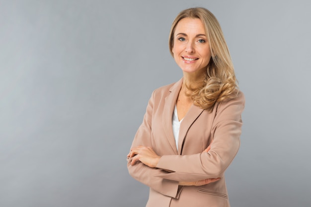 Free photo smiling portrait of a confident blonde young woman standing against gray backdrop