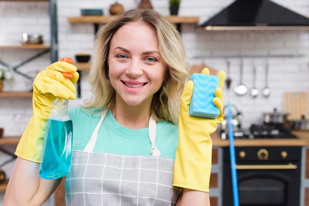 Smiling portrait of a female janitor holding spray bottle and cleaning sponge